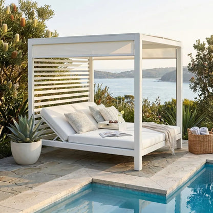 White outdoor daybed with cushions by a poolside, overlooking a scenic landscape.