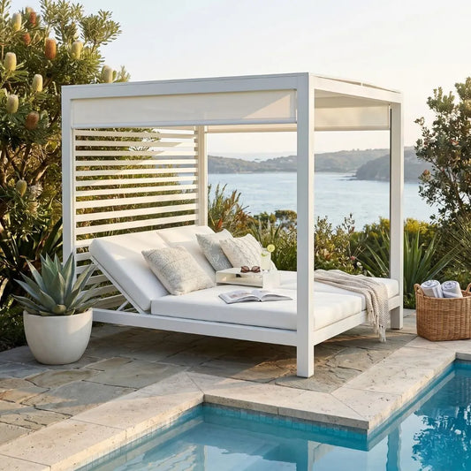 White outdoor daybed with cushions by a poolside, overlooking a scenic landscape.