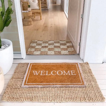 Doormat with text on a wooden floor, leading into a home.