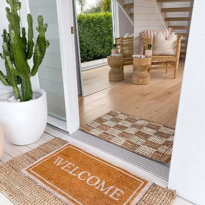 Welcome mat with text on a wooden floor, potted cactus, and outdoor furniture.