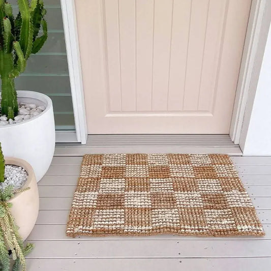 Patterned doormat on a wooden deck with a door and potted plants in the background