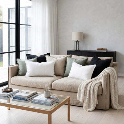 Beige sofa with decorative pillows and a blanket in a modern living room.