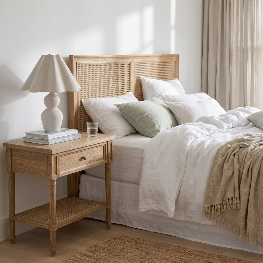 Neatly made bed with wooden headboard and side table in a bright bedroom.