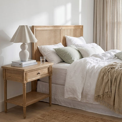 Neatly made bed with wooden headboard and side table in a bright bedroom.