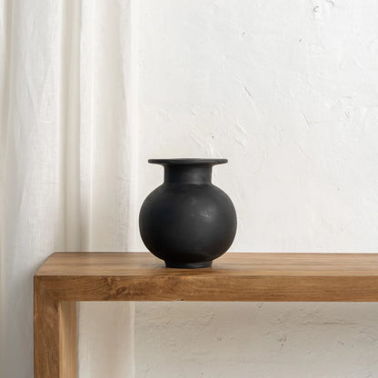 Black vase on a wooden table with a white curtain in the background