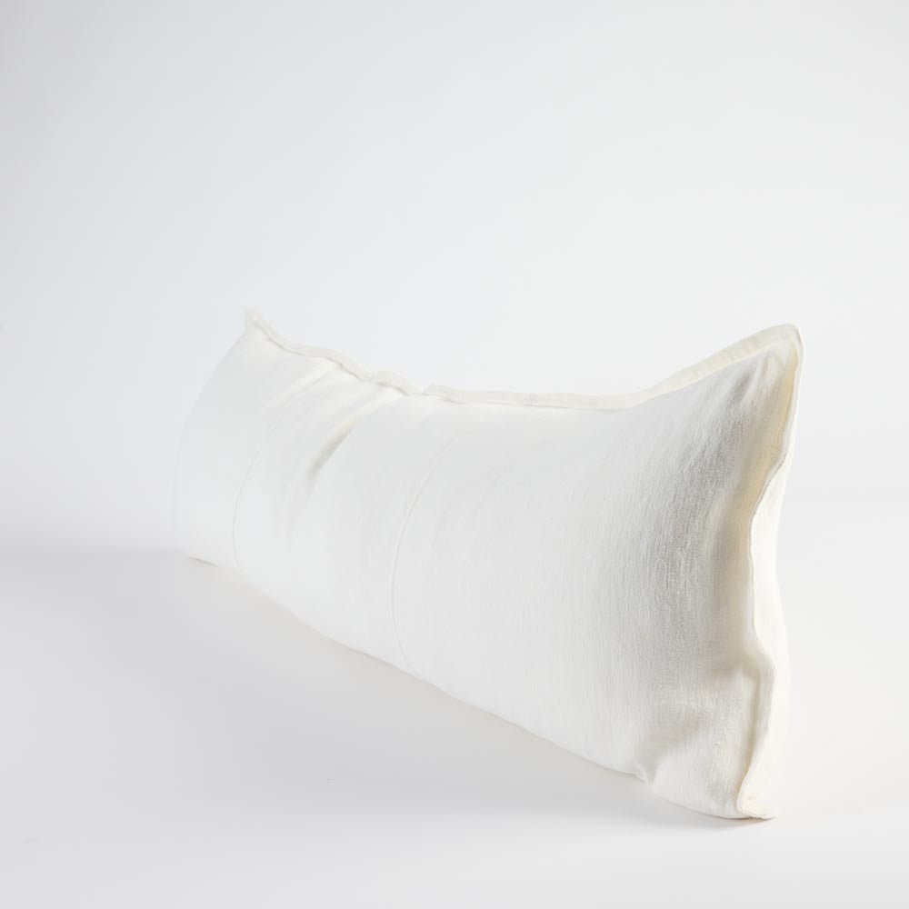 A long, rectangular lumbar pillow in a natural off-white linen fabric, shown at an angle on a seamless light gray studio background.
