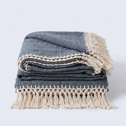 A folded dark gray woven throw blanket with cream-colored fringe and decorative crochet trim, displayed on a clean white background.