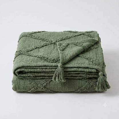 An olive green textured throw blanket with a diamond quilted pattern and matching tassels, folded neatly on a light gray background.