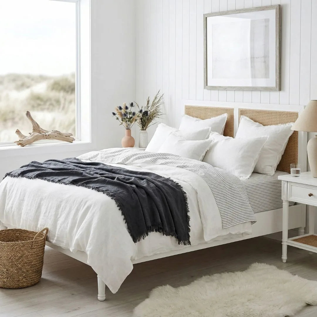 Neatly made bed with white bedding and a black throw blanket in a bright bedroom.