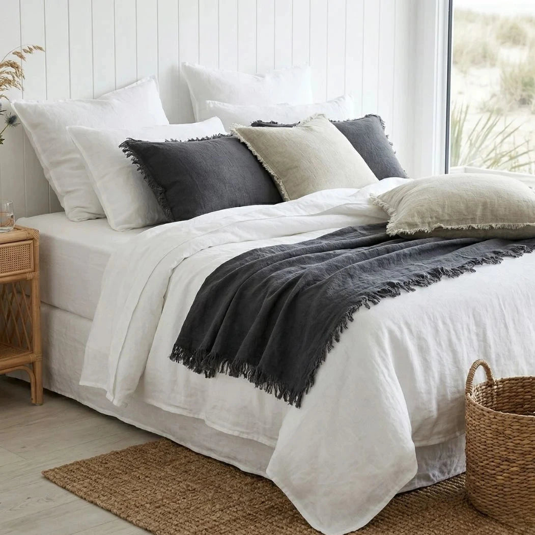 Neatly made bed with white bedding and gray throw blanket in a bright bedroom.
