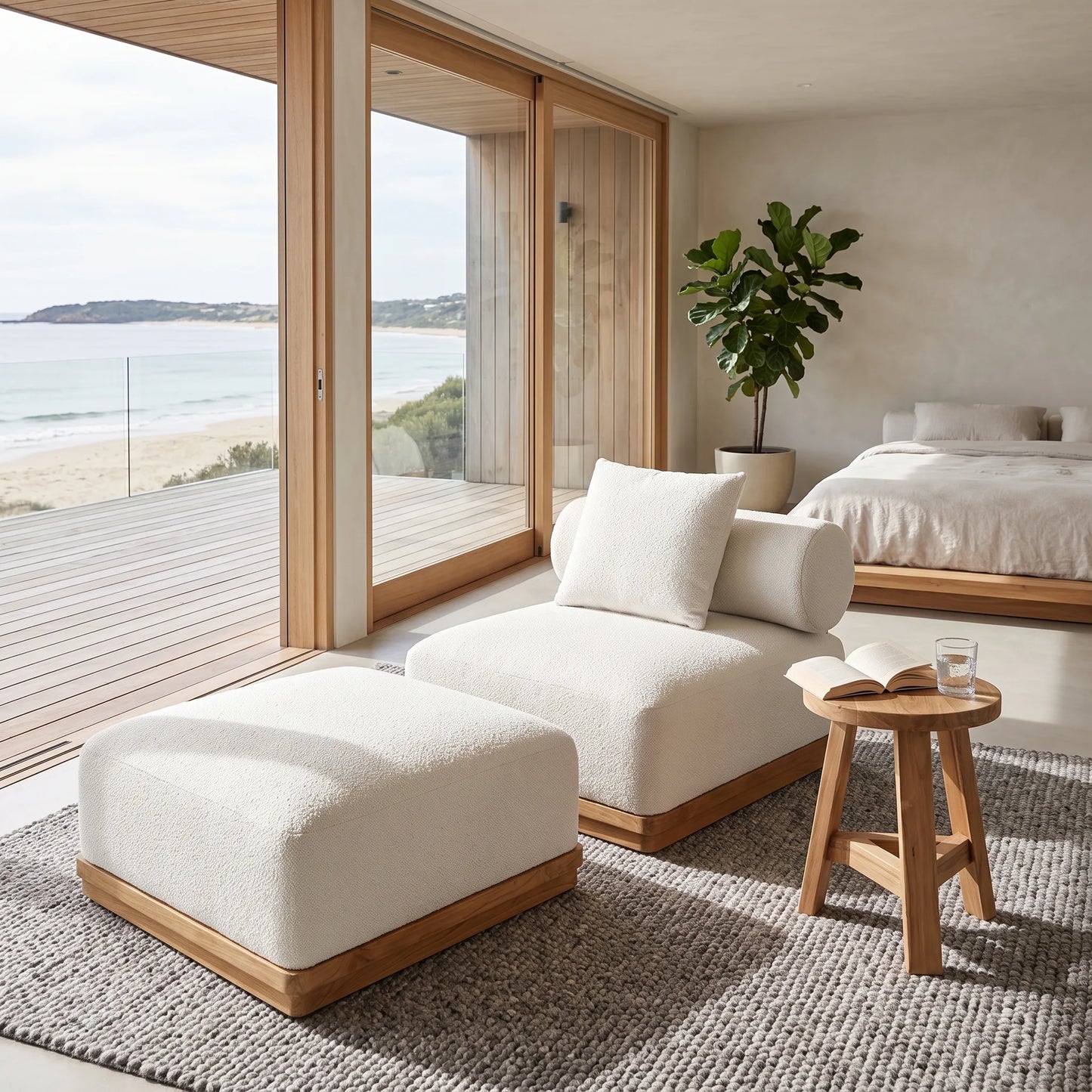 A modern beachfront lounge chair and matching ottoman in textured off-white bouclé fabric with light wood bases, styled in a minimalist coastal bedroom setting.