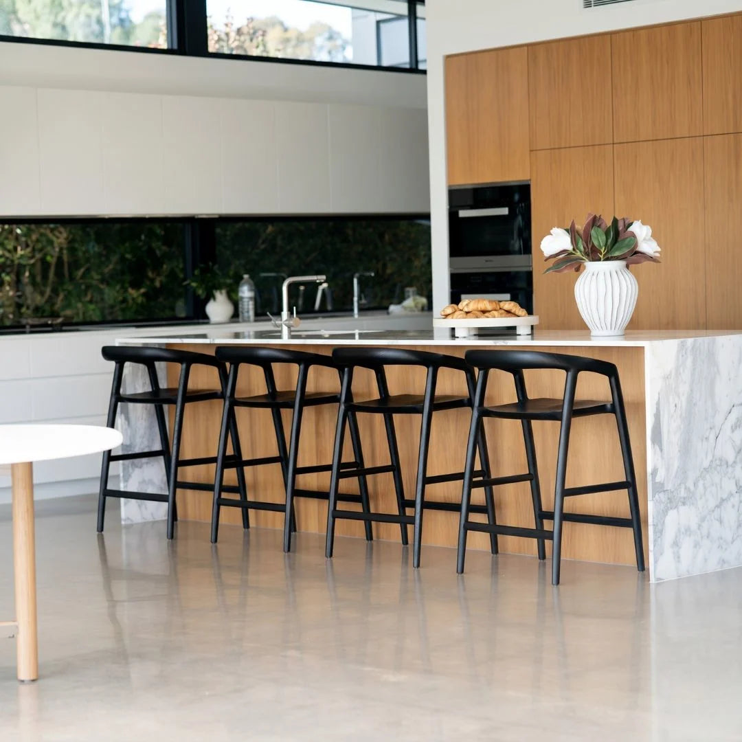 Modern kitchen with black bar stools, white marble countertop, and wooden cabinets.