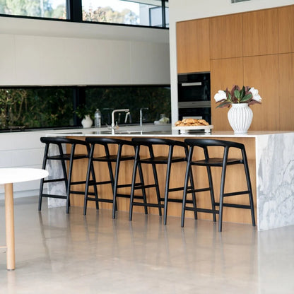 Modern kitchen with black bar stools, white marble countertop, and wooden cabinets.
