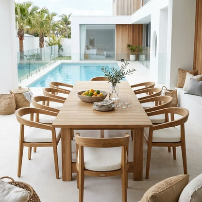 A modern dining set with a rectangular light wood table and matching curved-back chairs with white cushions, styled in a bright, contemporary outdoor patio setting next to a swimming pool.