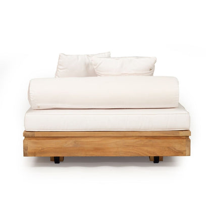 A modern outdoor daybed featuring a natural teak wood frame, a thick cream-colored mattress, a matching rolled lumbar pillow, and two square back pillows, shown against a solid white background.