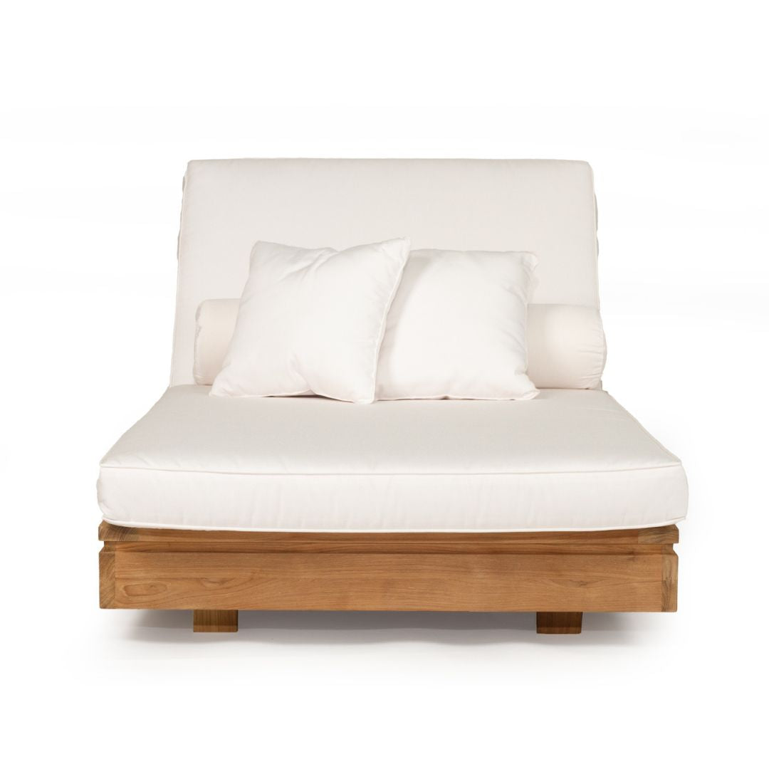 A modern outdoor daybed featuring a light brown wooden frame, a thick off-white cushioned mattress, a tall upholstered backrest, and two matching off-white throw pillows, shown against a plain white background.
