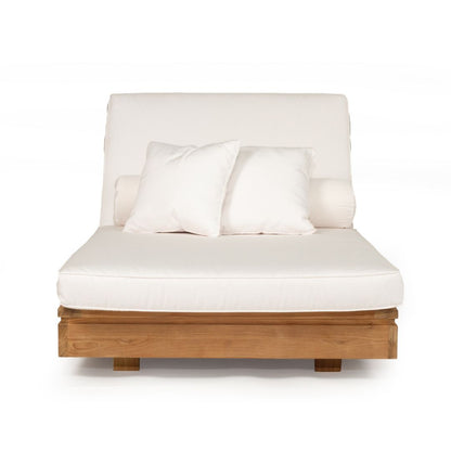 A modern outdoor daybed featuring a light brown wooden frame, a thick off-white cushioned mattress, a tall upholstered backrest, and two matching off-white throw pillows, shown against a plain white background.