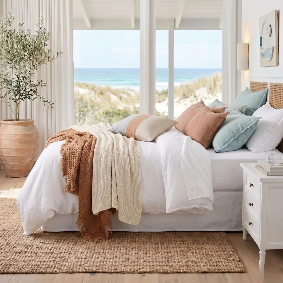 Bedroom with a view of the ocean, featuring a bed with colorful pillows and a plant.