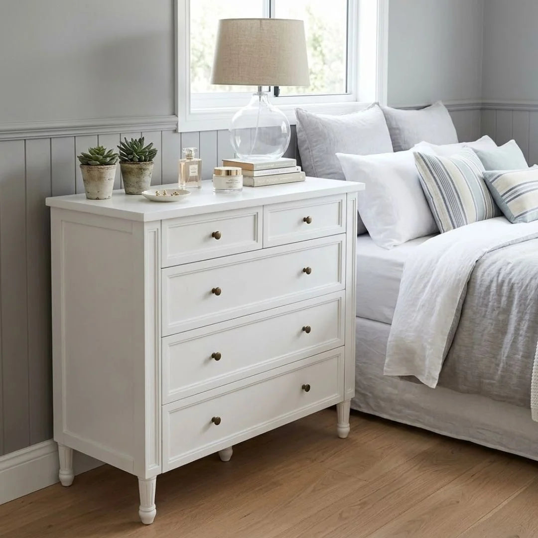 White dresser with decorative items next to a bed with striped bedding in a bedroom.