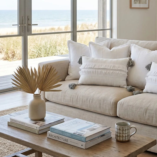 Beige sofa with decorative pillows in a living room with large windows showing a beach view.