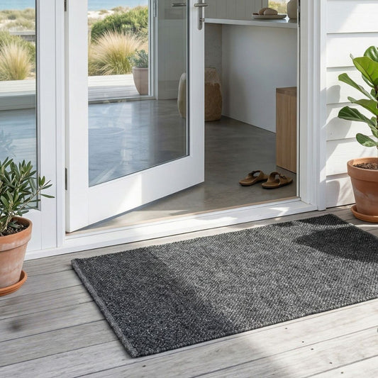 Grey Eco doormat on a wooden deck with a glass door leading to a patio.