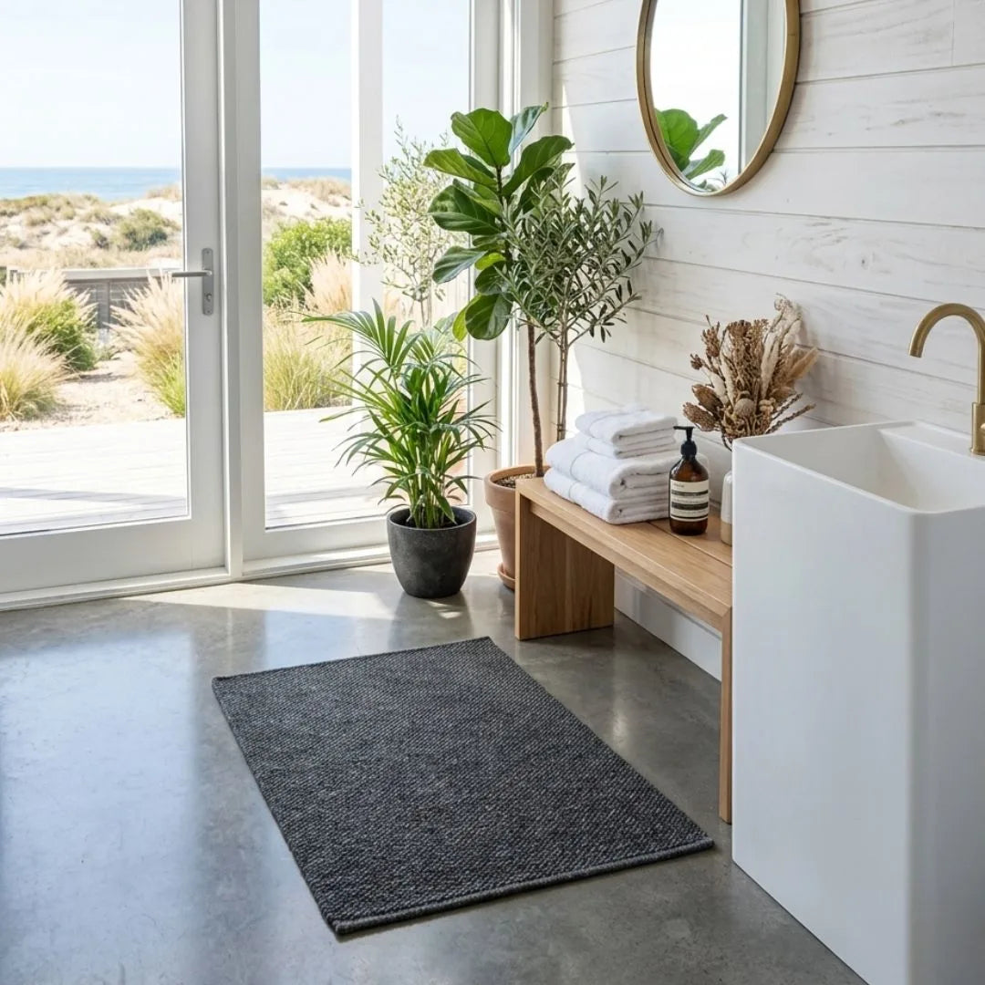 Modern bathroom with a sink, towel, and plants near a large window with a view of the ocean.