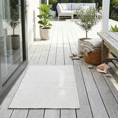Outdoor patio with wooden deck, rug, plants, and seating area.