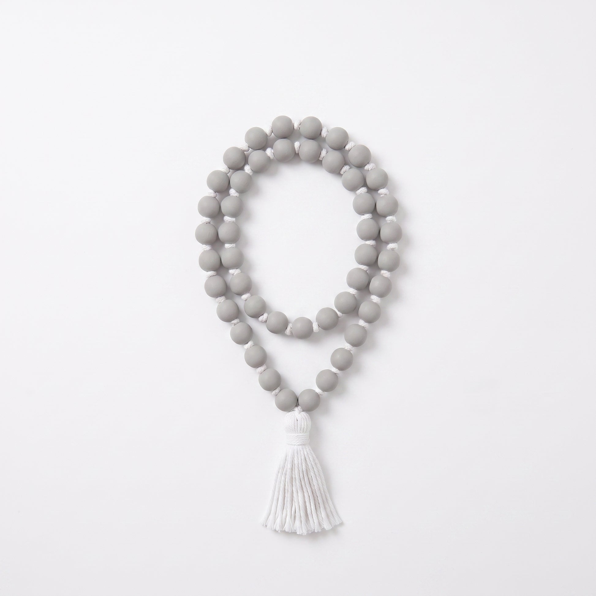 A double-strand beaded necklace with matte gray round beads and a white tassel, displayed on a clean white background.