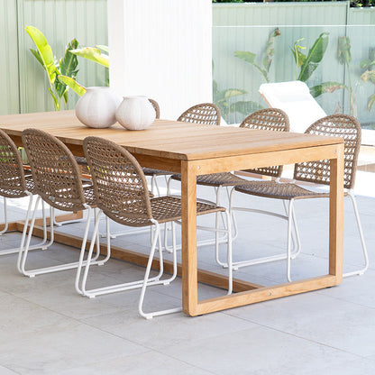 A modern 7-piece dining set featuring a rectangular light oak wood table and six woven wicker chairs with white metal legs, styled in a bright, contemporary patio dining area.