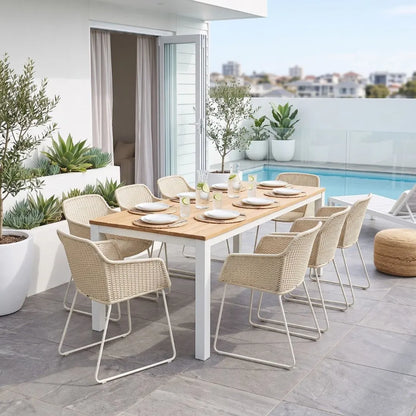 An outdoor dining set on a modern patio, featuring a rectangular wooden table with white metal legs and eight woven beige armchairs with white metal frames, set next to a swimming pool.