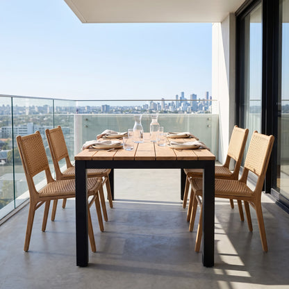 Outdoor dining set on a balcony featuring a rectangular wooden table with black legs and four matching woven-back chairs, set against a city skyline background.