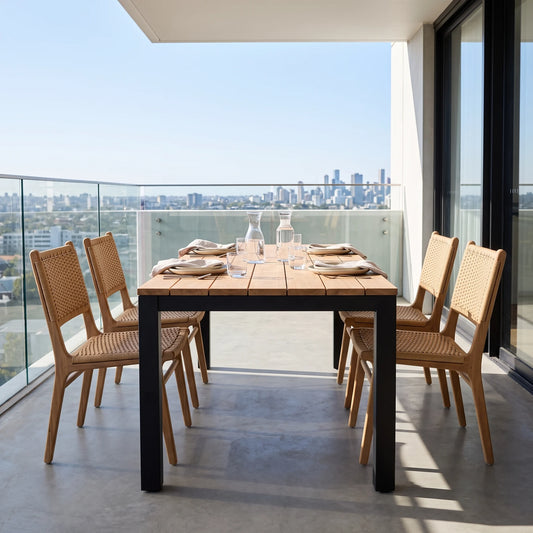 Outdoor dining set on a balcony featuring a rectangular wooden table with black legs and four matching woven-back chairs, set against a city skyline background.