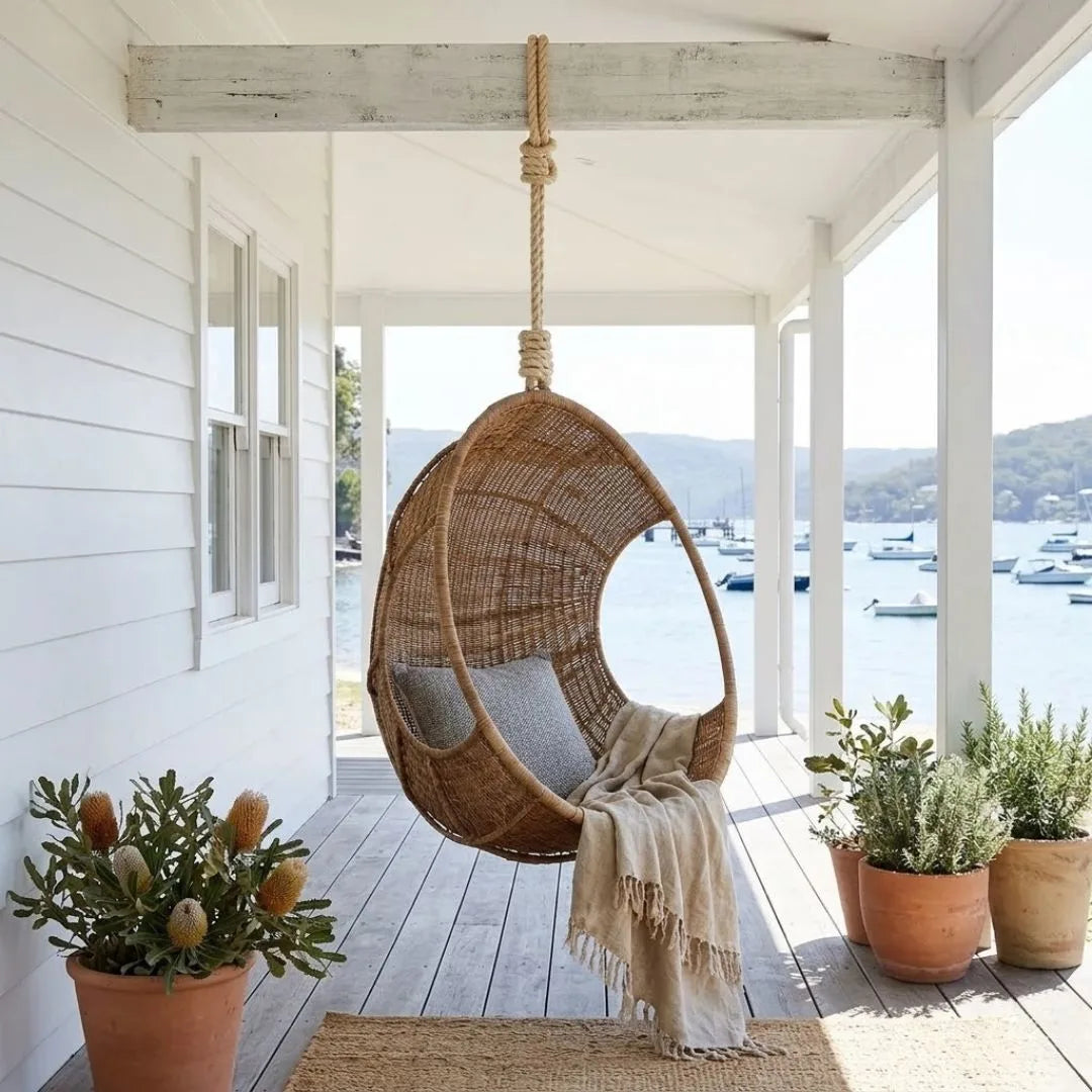 Woven egg chair on a porch with potted plants and a view of boats.