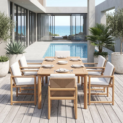 A 7-piece outdoor dining set on a light wood deck overlooking a swimming pool and ocean view. The set includes a rectangular light wood table with white plates and silver cutlery, surrounded by six matching armchairs with white cushions and light wood frames.