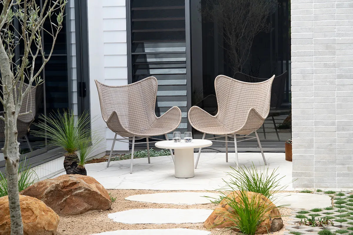 Two wicker chairs with a small table on a patio area in front of a house.