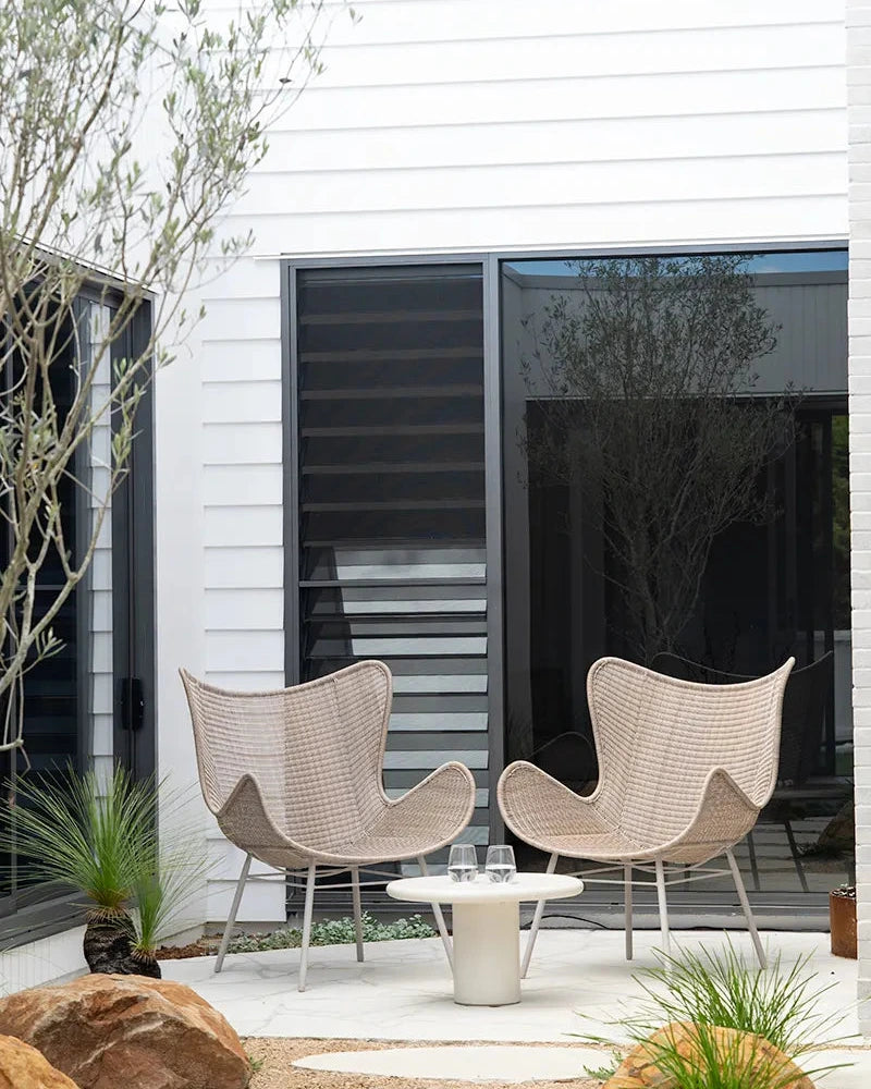 Two wicker chairs and a small table on a patio in front of a modern house.