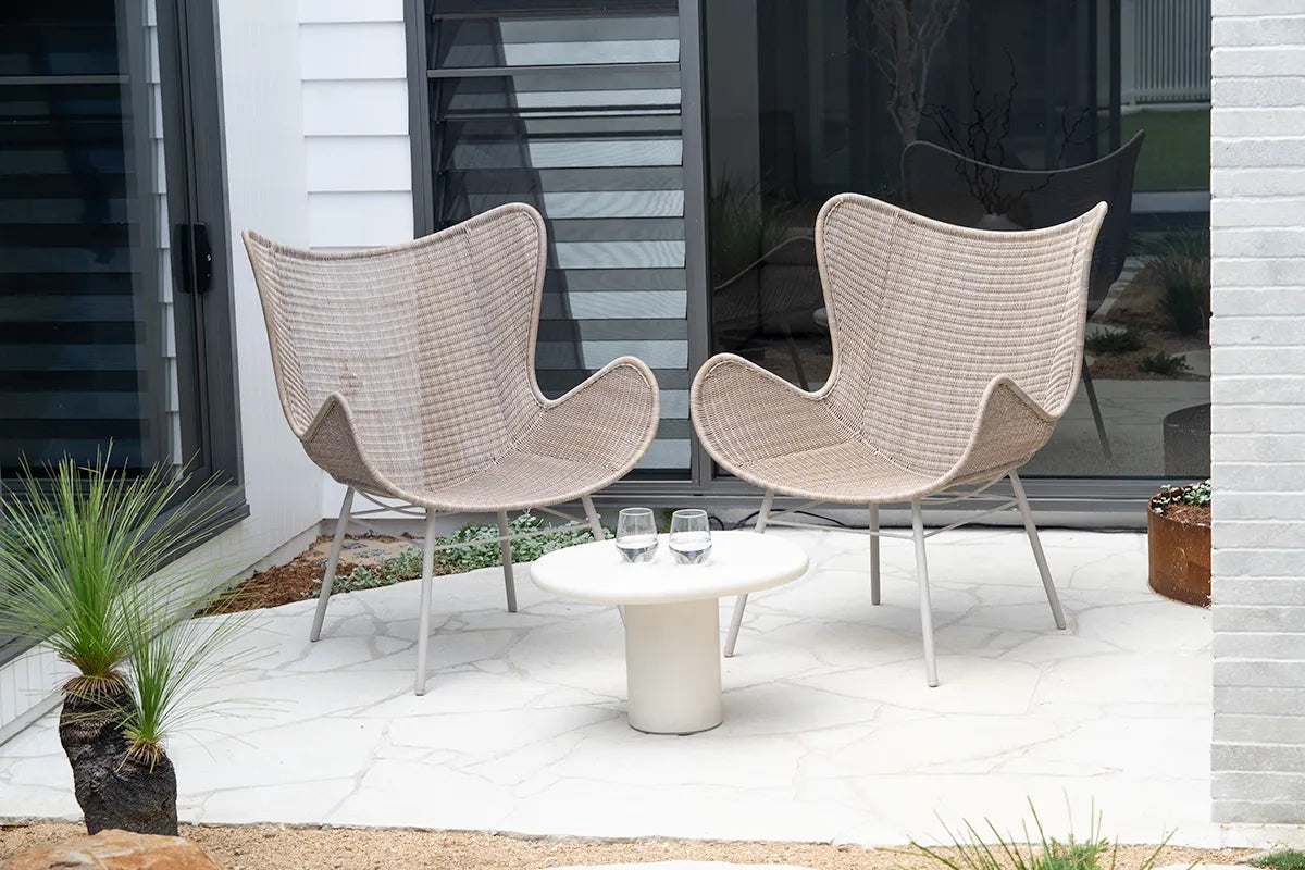 Two wicker chairs and a small table on a patio with a modern building in the background.