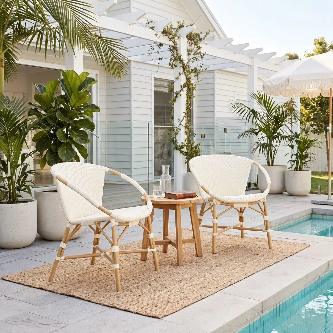 A 3-piece outdoor patio furniture set featuring two cream mesh sling chairs with natural wood frames and a matching small wooden side table, arranged on a jute rug next to a swimming pool.