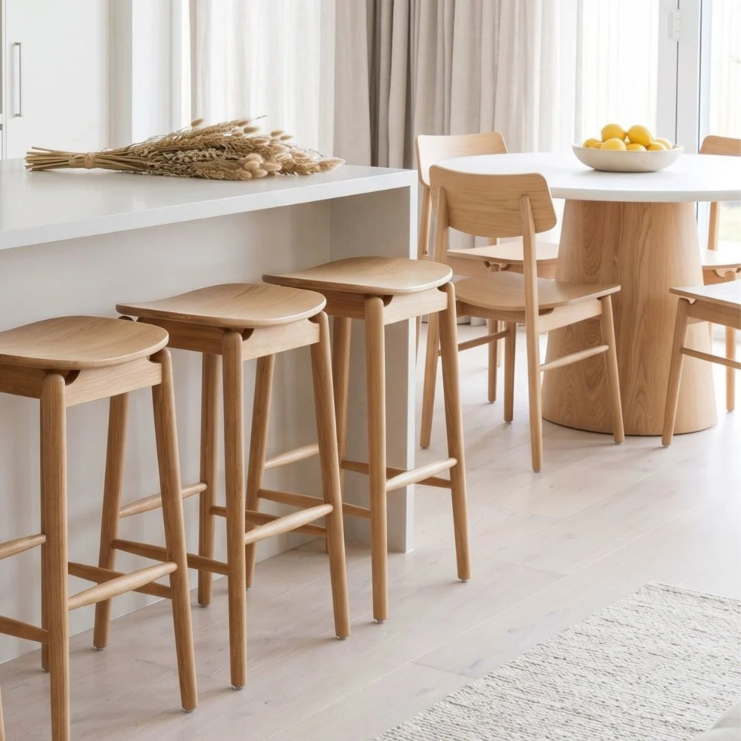 Wooden bar stools and chairs in a modern kitchen setting with a white countertop and light-colored floor.