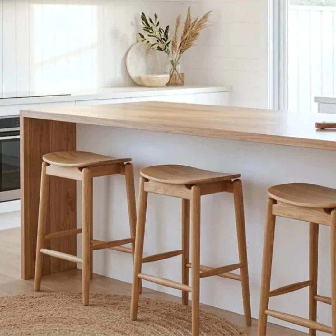 Wooden bar stools in a modern kitchen setting with white countertops and neutral decor.