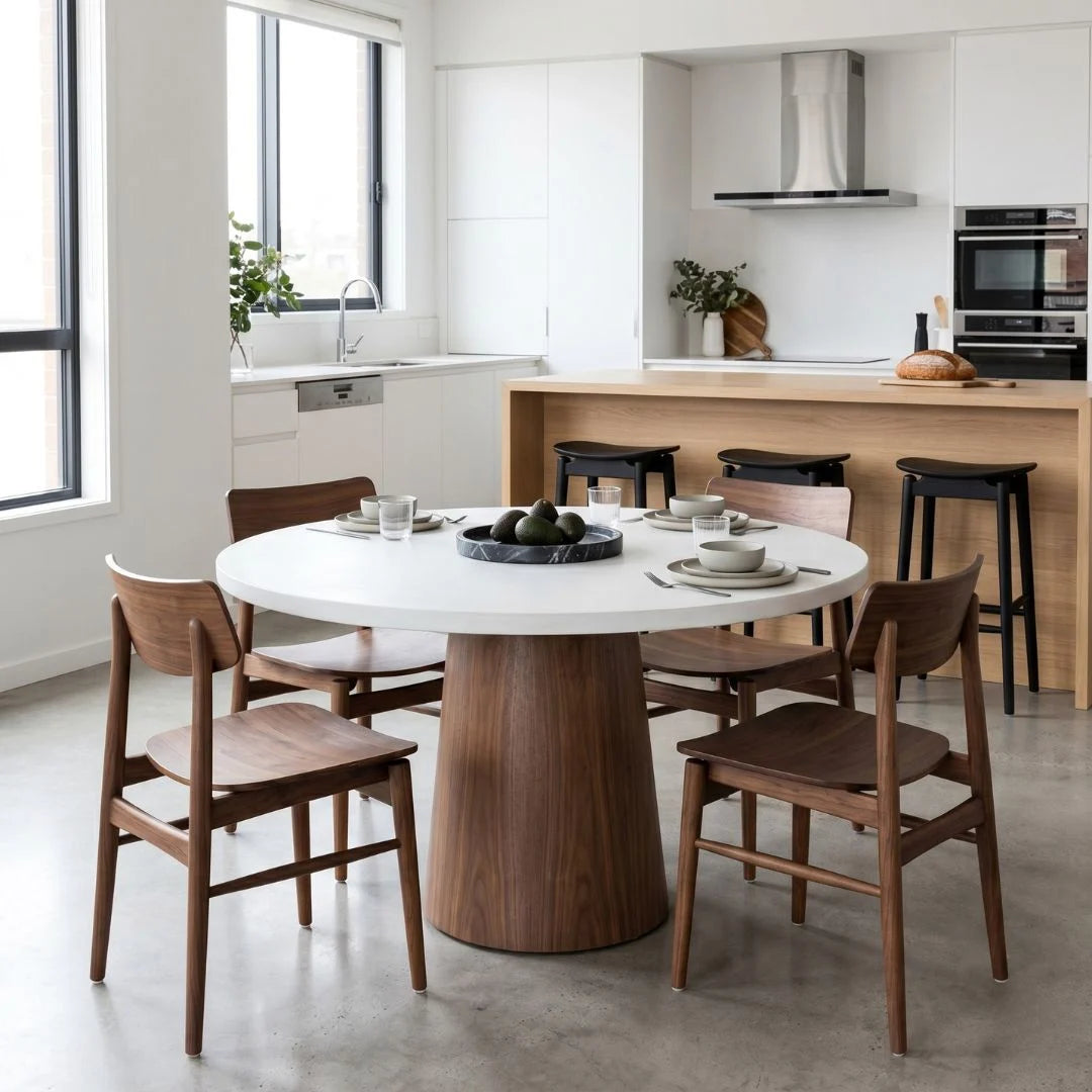 Jansen microcement round dining table with walnut base, matching walnut jansen dining chairs and black counter stools in a modern apartment.