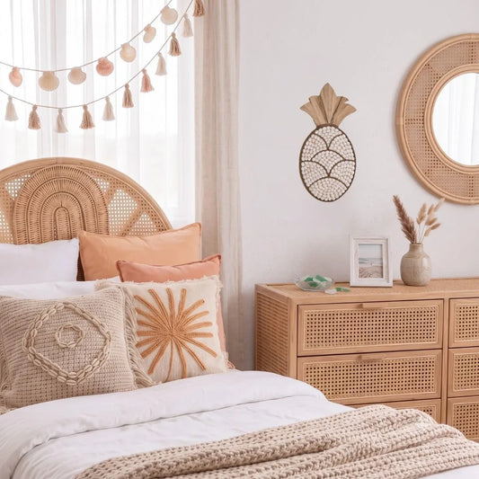 A bohemian-style bedroom featuring a rattan headboard, a matching rattan dresser, a woven pineapple wall decor piece, and neutral-toned bedding with decorative throw pillows.