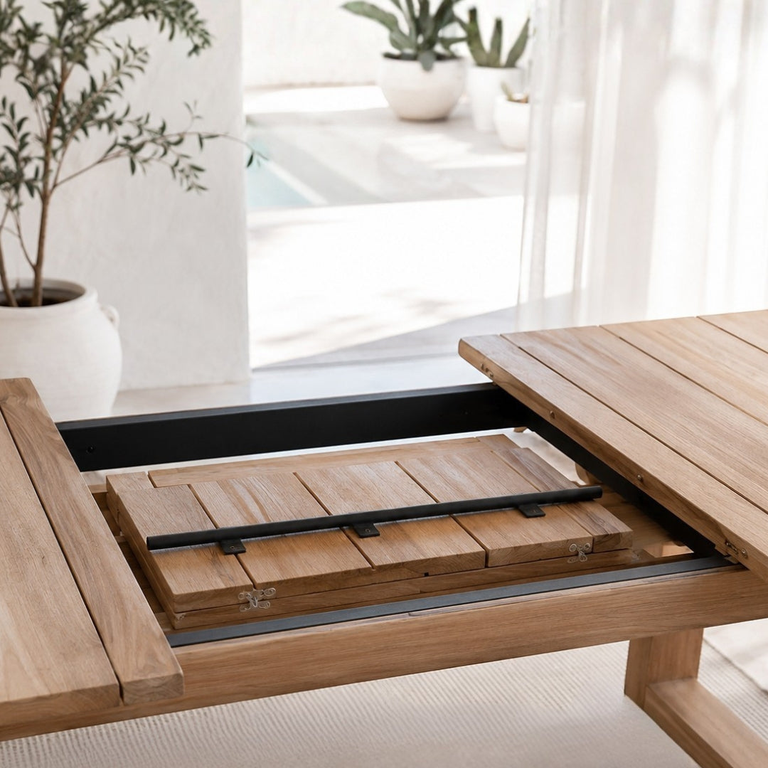 A close-up of a wooden outdoor dining table with a extension showing the slat and black metal guide rails in a bright, modern patio setting.