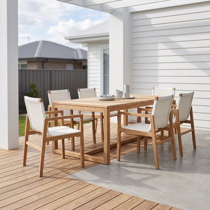 A 7-piece outdoor dining set with a rectangular light oak table and six matching armchairs with woven rope backs and cream cushions, set on a wooden deck under a covered patio.