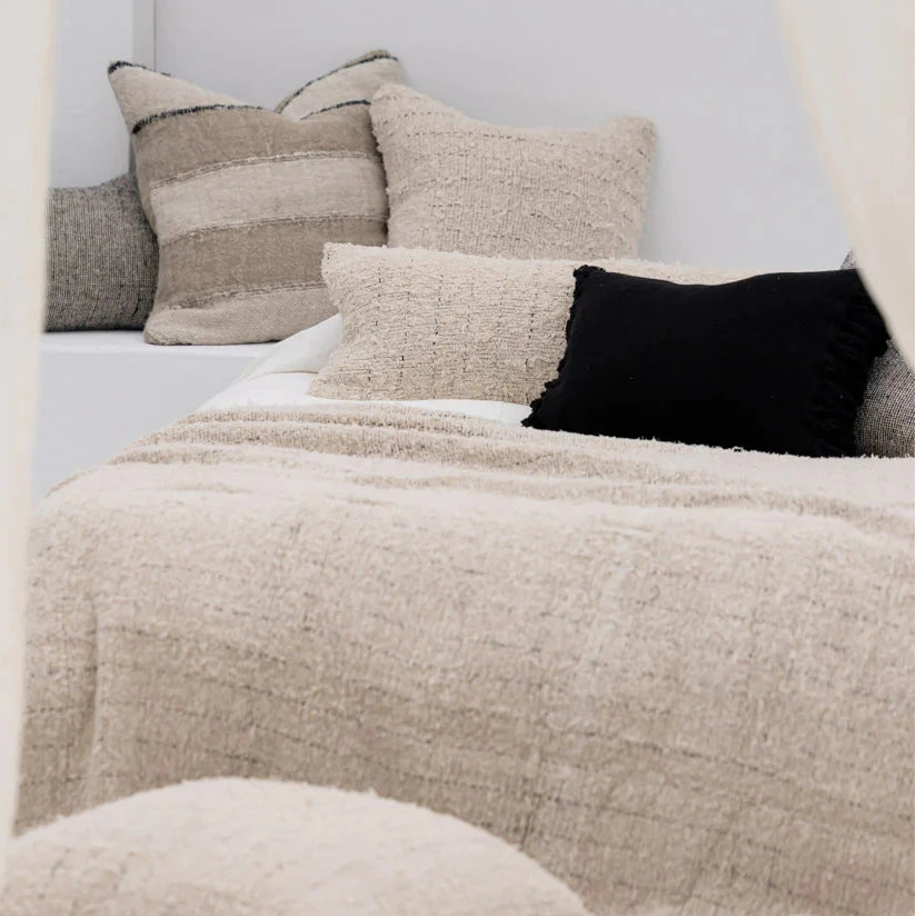 Neatly arranged pillows on a bed with a textured beige blanket.