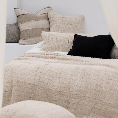 Neatly arranged pillows on a bed with a textured beige blanket.