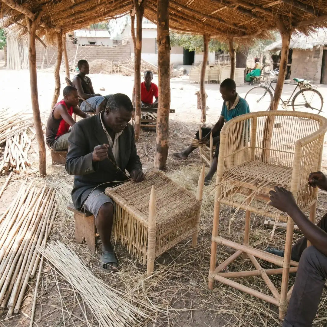 People working with woven materials under a thatched roof structure.