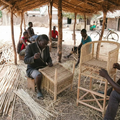People working with woven materials under a thatched roof structure.