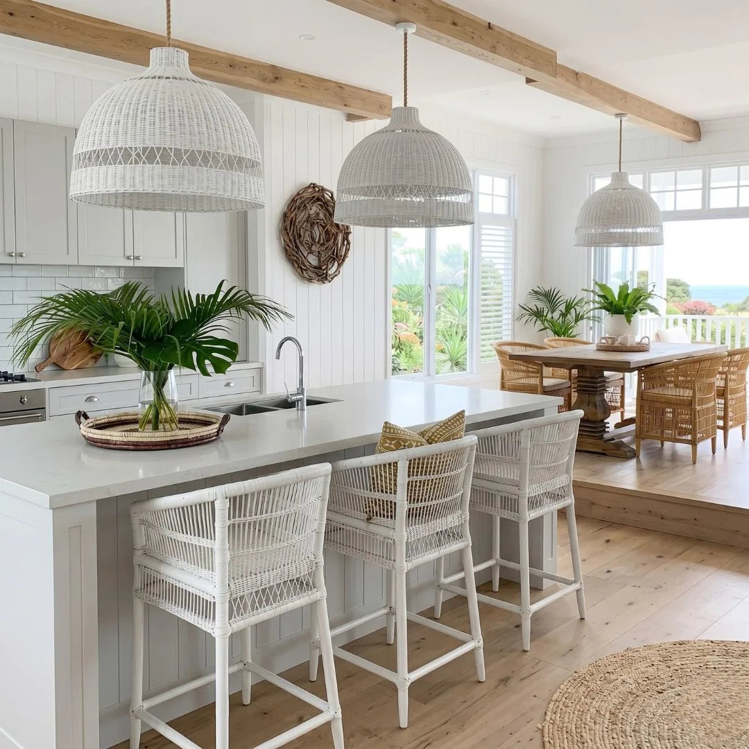 Modern kitchen with white island, stools, and pendant lights with a view of a garden.