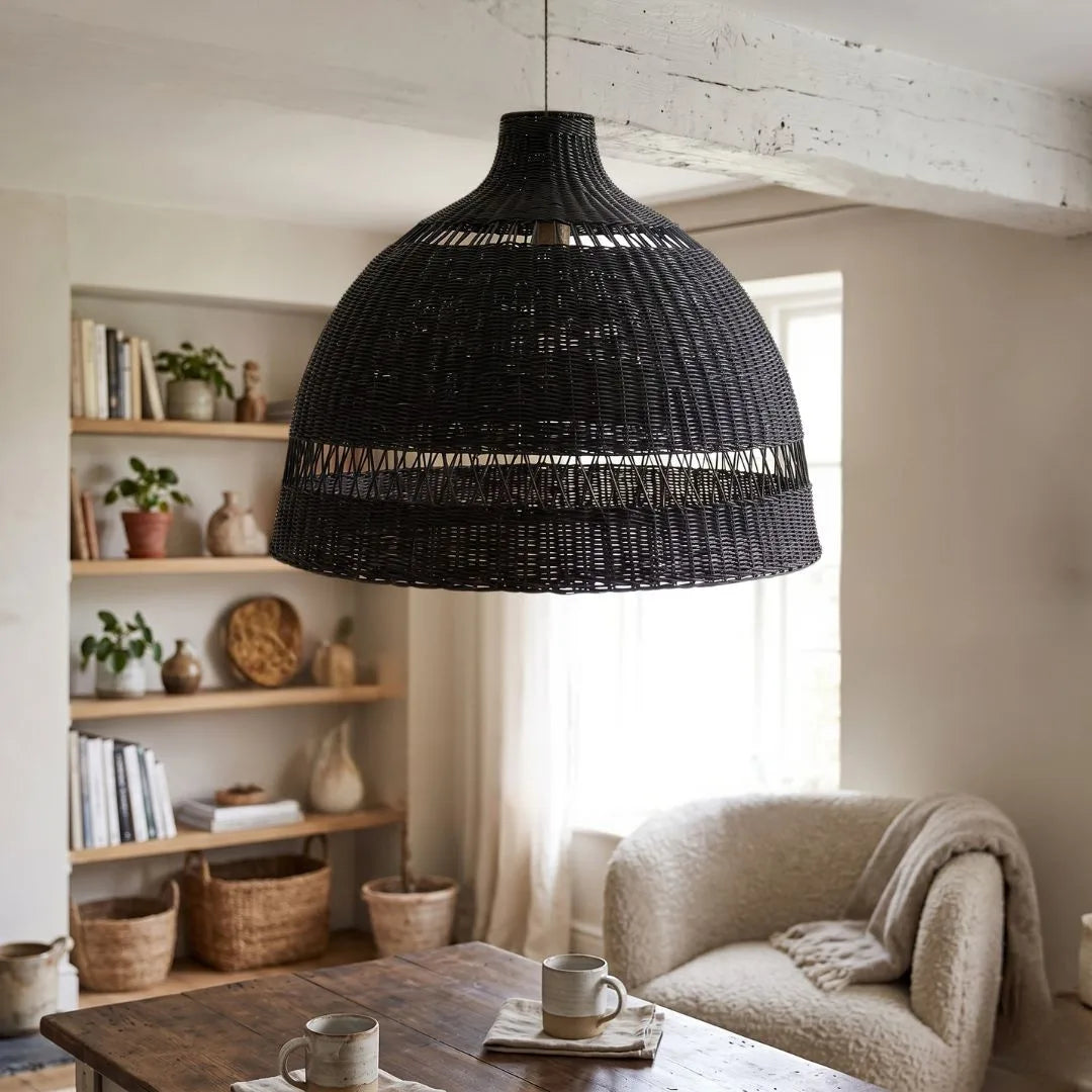 Black woven pendant light hanging in a living room with a sofa and bookshelf.